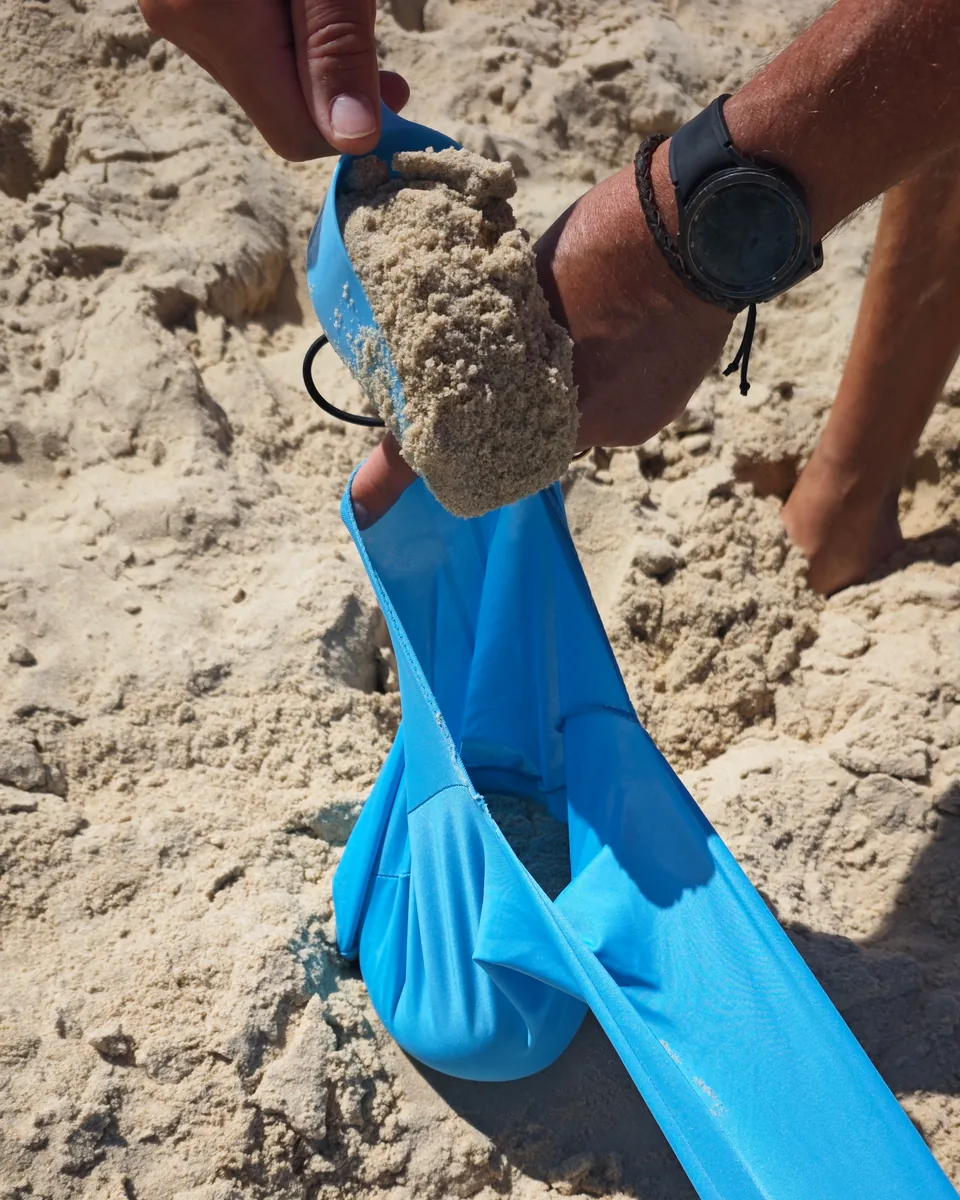 Hand befüllt eine der Sandtaschen des CUUPO Sonnensegels mit Sand