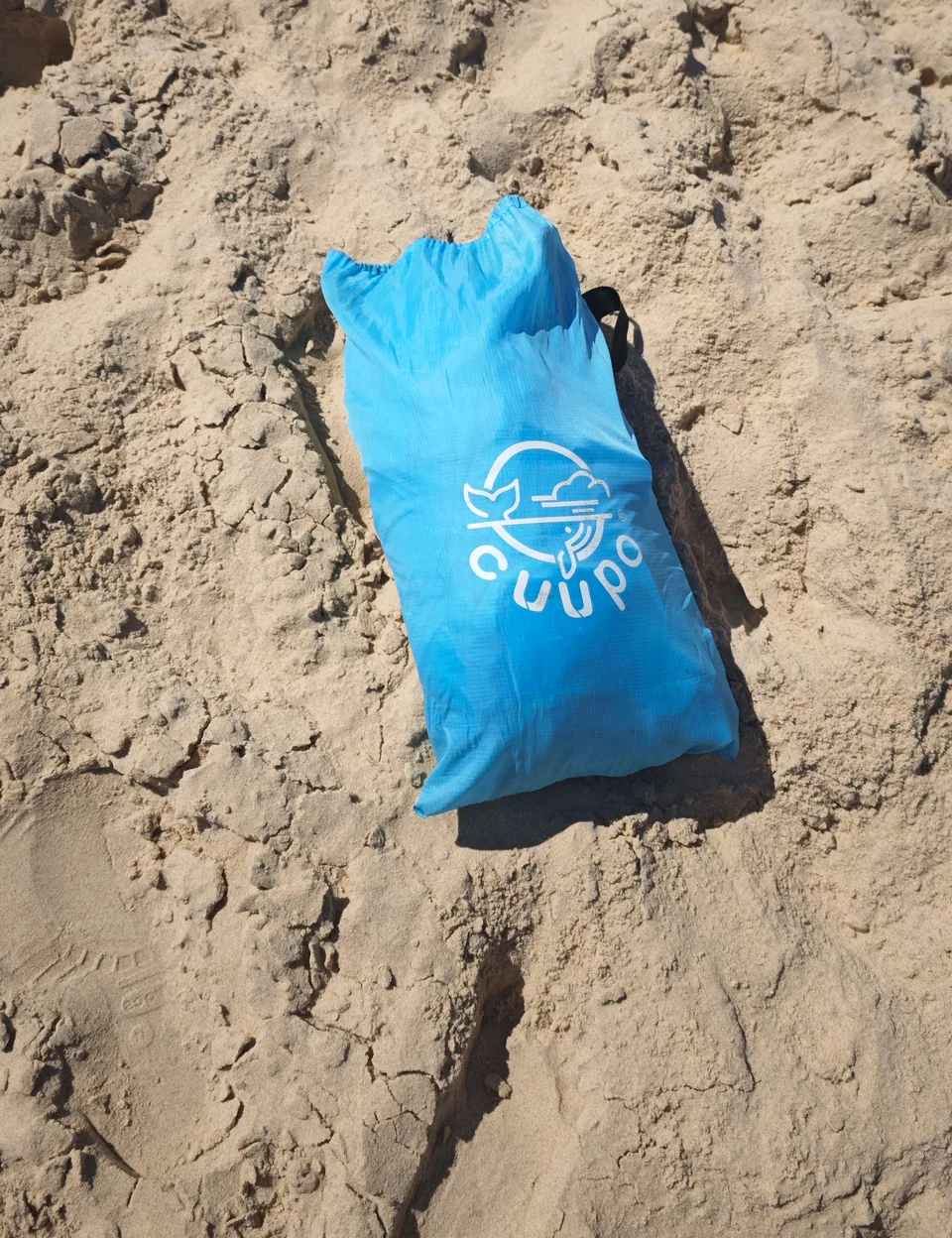 Zusammengepackter CUUPO-Transportbeutel mit Logo im Sand