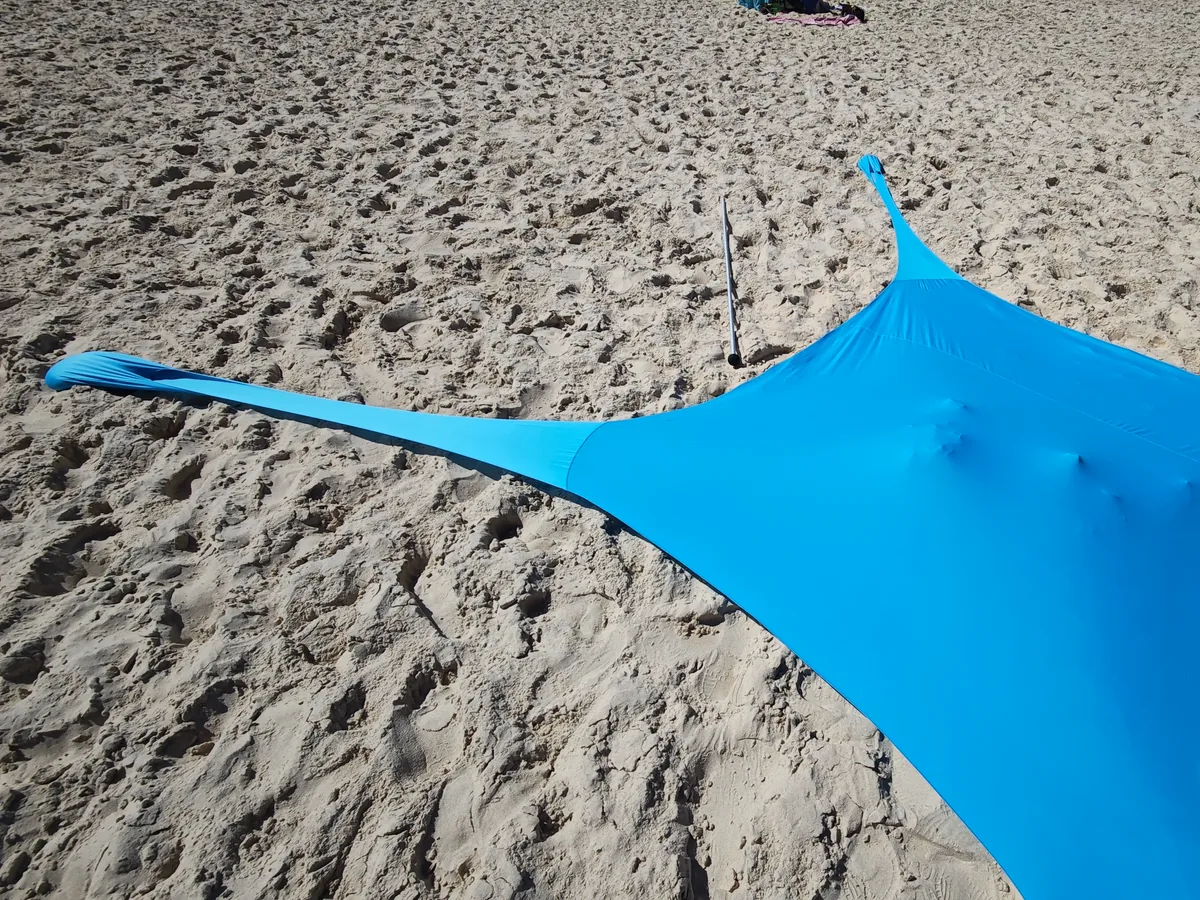 Vollständig aufgebautes blaues CUUPO Sonnensegel von schräg oben am Sandstrand